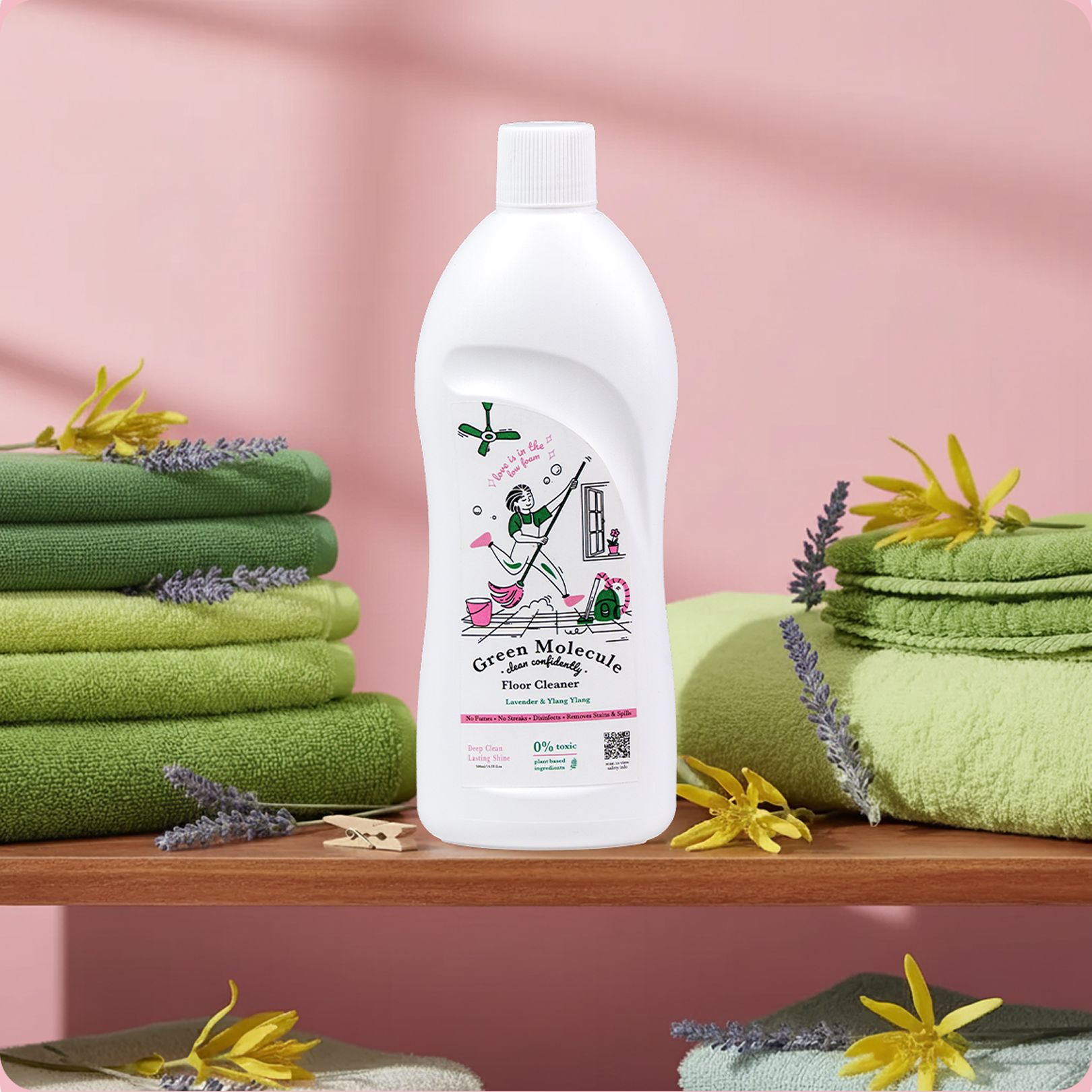 Green Molecule Floor Cleaner bottle displayed on a wooden shelf with neatly folded green towels, lavender sprigs, and yellow flowers against a soft pink background.